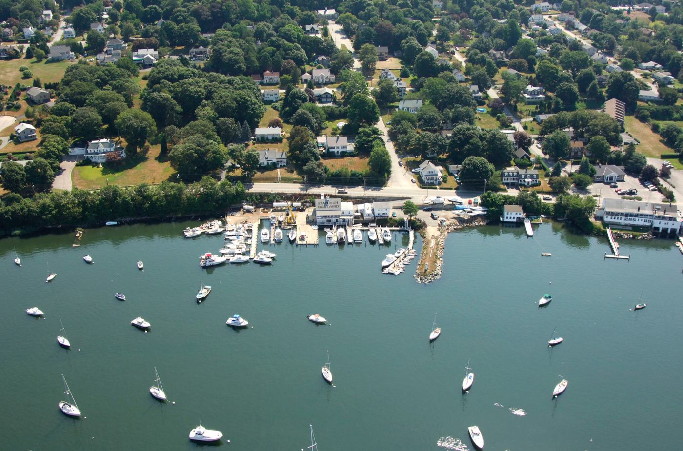 Earlier aerial view of Standish Boat Yard with its name painted on the roof, the docks, the breakwater and the mooring field