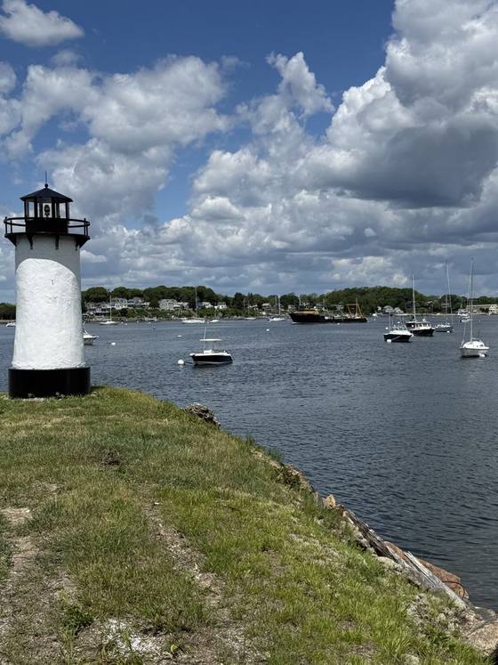 The white Standish lighthouse on the jetty, with moored boats on the Sakonnet behind it