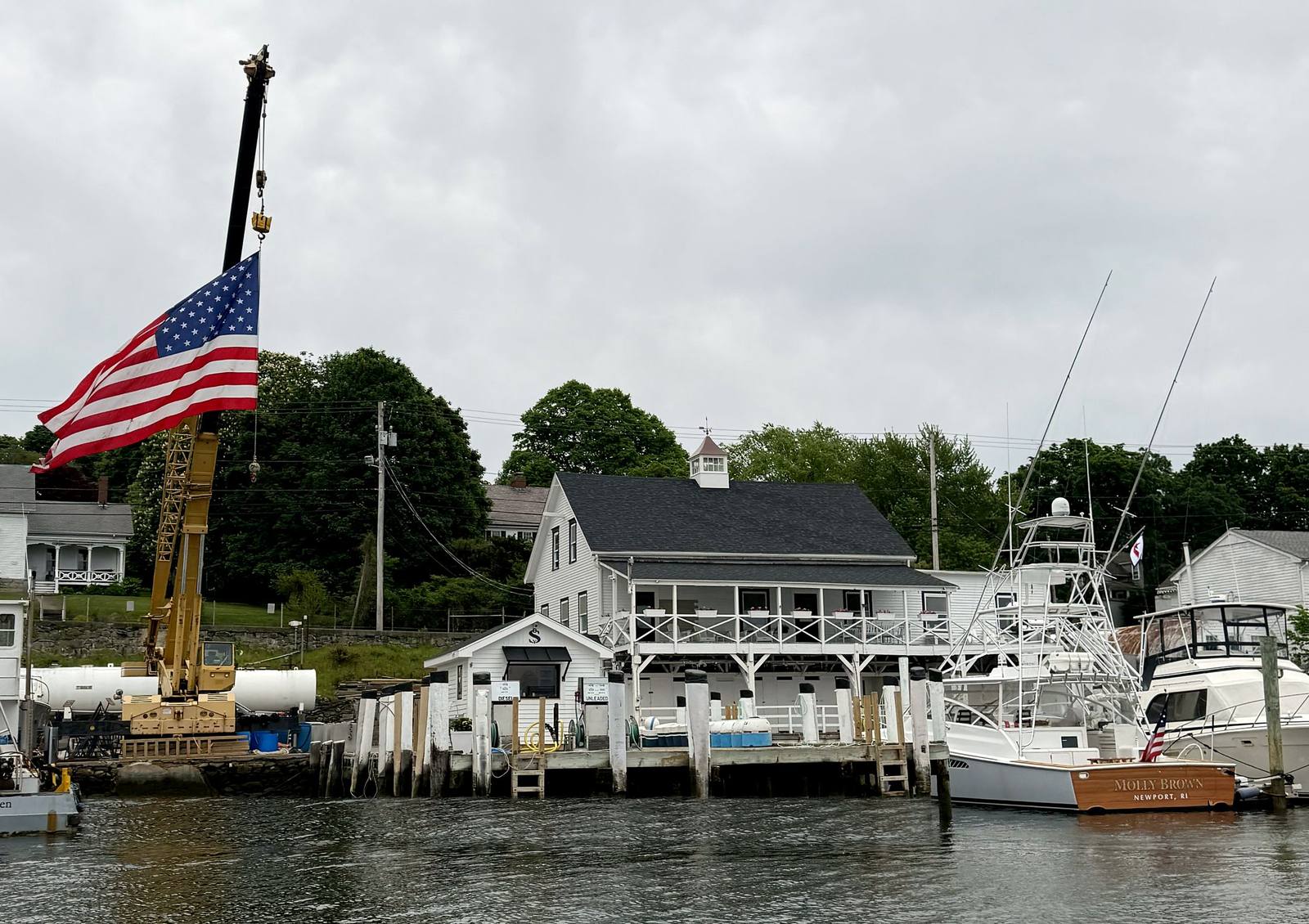 The Standish fuel dock and ship store from the water, with the crane flying an American flag and sportfishing boats at the docks